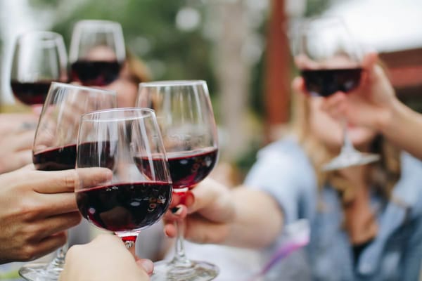 Hands toasting with glasses of red wine, outdoor setting. Close-up of celebratory gathering.