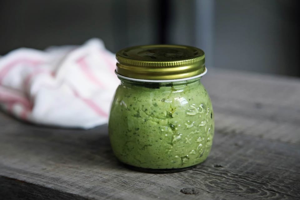 A jar of homemade pesto sauce on a wooden surface